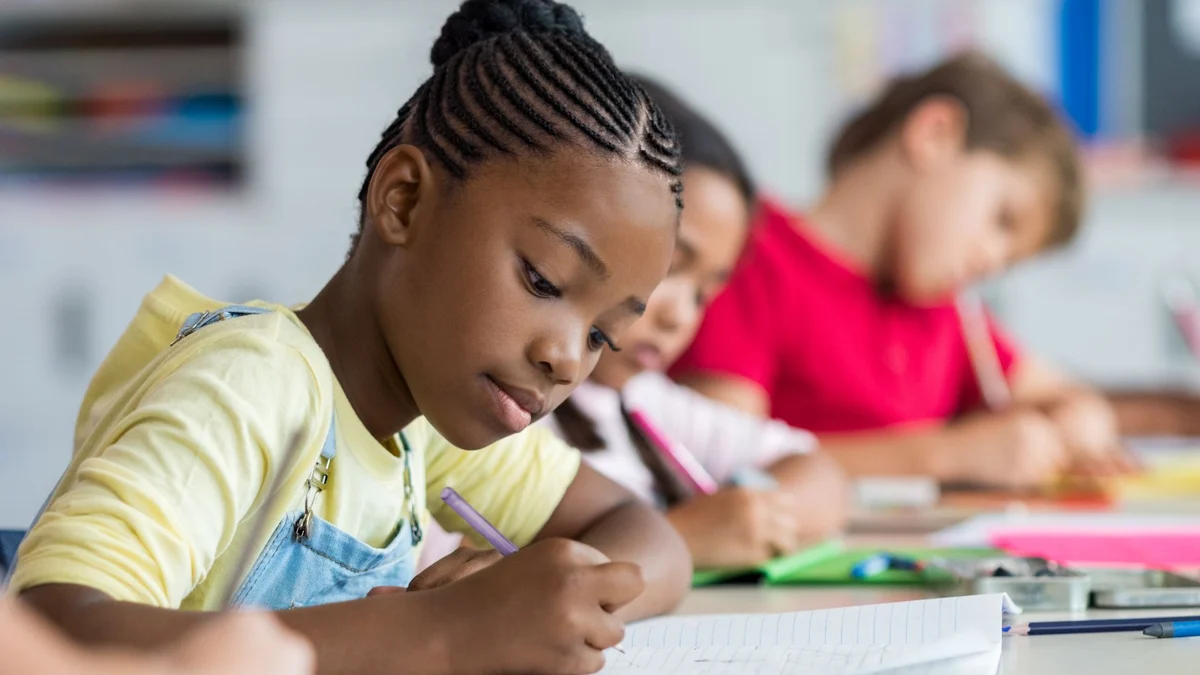 A child writing in a notebook alongside classmates.