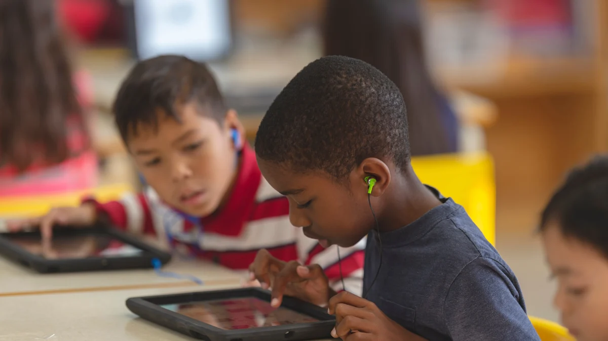 Children using tablets and earphones at a classroom table.