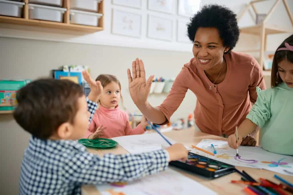 An educator giving a child a high-five during an art activity with other children.