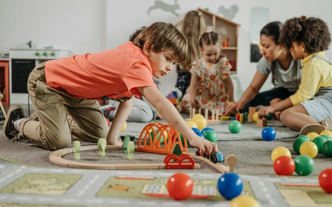 Children and an adult playing together with a wooden train set and toys.